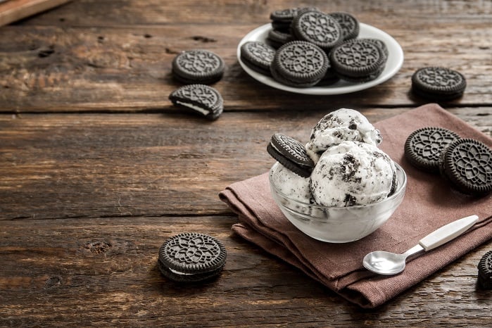Allnutrition Nutlove Crispy Cookie, a cookies and cream dessert with chocolate sandwich cookies and creamy filling, shown with scoops of cookies and cream ice cream in a glass bowl on a rustic wooden table.
